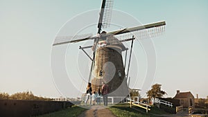 Family of four stand by huge old Dutch wind mill. Amazing shot of people before an architecture landmark. Back view. 4K.