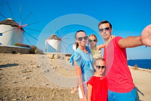 Family of four taking selfie with a stick in front of windmills at popular tourist area on Mykonos island, Greece