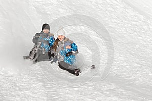 A family of four with the twins slide down a snow hill in winter in the Park