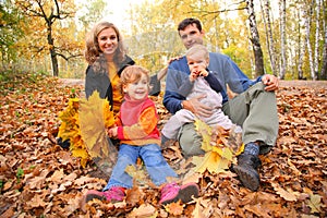 Family of four with yellow leaves sits in wood