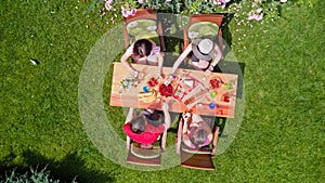 Family and friends eating together outdoors on summer garden party. Aerial view of table with food and drinks from above