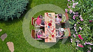 Family and friends eating together outdoors on summer garden party. Aerial view of table with food and drinks from above