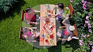 Family and friends eating together outdoors on summer garden party. Aerial view of table with food and drinks from above