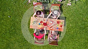 Family and friends eating together outdoors on summer garden party. Aerial view of table with food and drinks from above