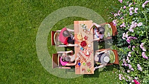 Family and friends eating together outdoors on summer garden party. Aerial view of table with food and drinks from above