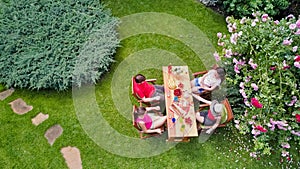 Family and friends eating together outdoors on summer garden party in park. Aerial view of table with food and drinks