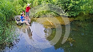 Family and friends fishing together outdoors near lake in summer, aerial top view from above