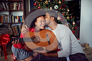 Family in front of decoration Christmas tree. man surprise woman a with a guitar gift for Christmas