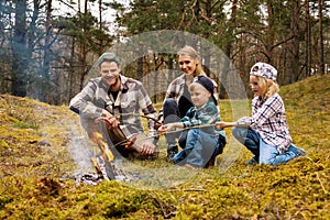 family frying sausages over a bonfire while camping in forest. family time, nature adventure