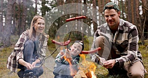 family frying sausages over a campfire in the forest. nature picnic, camping