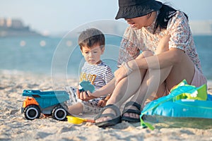 Family Fun on a Beach Vacation. Mother playing with a toy truck and the sand on the beach with her baby boy