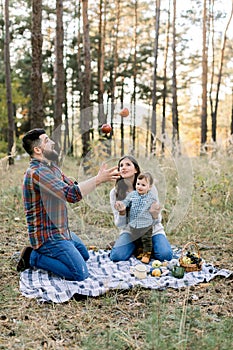 Family, fun and leisure concept. Portrait of happy family sitting on checkered plaid in autumn forest. Pretty mom and