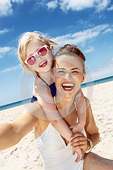 Mother and daughter in swimsuits taking selfies at beach