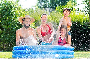 Family in garden pool cooling down splashing water