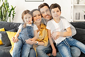 Family garmony. Happy multiracial family of four sitting on the sofa in cozy living room