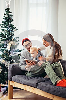 Family gathered around a Christmas tree, using a tablet