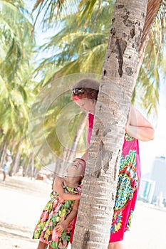 Family, generation - happy smiling grandmother and little granddaughter stand near the palm on the beach