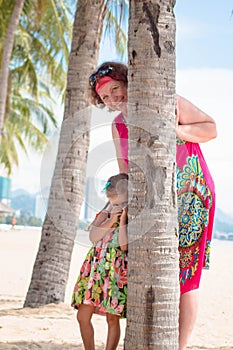 Family, generation - happy smiling grandmother and little granddaughter stand near the palm on the beach