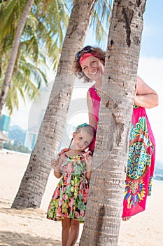 Family, generation - happy smiling grandmother and little granddaughter stand near the palm on the beach
