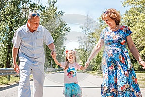 Family, generation and people concept - happy smiling grandmother, grandfather and little granddaughter walking at park