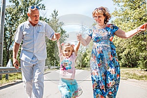 Family, generation and people concept - happy smiling grandmother, grandfather and little granddaughter walking at park