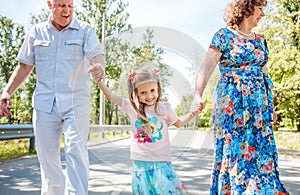 Family, generation and people concept - happy smiling grandmother, grandfather and little granddaughter walking at park