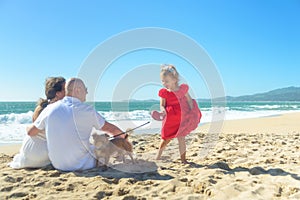 Family with girl in red dress and dog on the beach