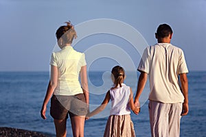 Family with girl walks along sea beach. Back view.