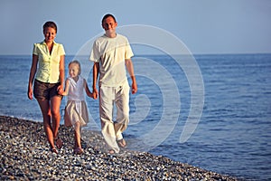 Family with girl walks along sunset sea beach