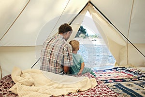 Family glamping. Father and his toddler son inside big camping tent with cozy interior. Luxury travel accomodation into the forest