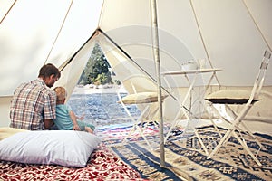 Family glamping outdoor vacation. Father and his toddler son inside big camping tent with cozy interior. Luxury travel photo