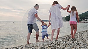 Family going to the beach in slow motion. Baby`s first steps on the sea shore.