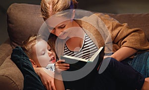 Family before going to bed mother reads to her child son book near a lamp