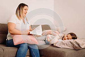 Family before going to bed mother reads to her child daughter book in the evening sitting on the sofa.