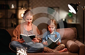 Family before going to bed mother reads to her child daughter book near a lamp in evening