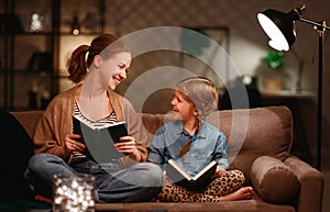 Family before going to bed mother reads to her child daughter book near a lamp in evening