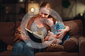 Family before going to bed mother reads to her child daughter book near a lamp in evening