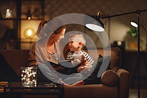 Family before going to bed mother reads to her child son book near a lamp in evening