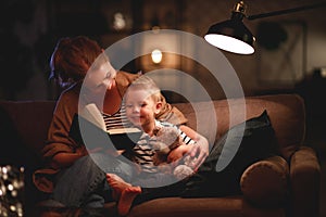 Family before going to bed mother reads to her child son book near a lamp in the evening