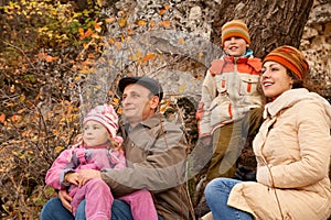 Family with grandfather sit on roots of trees