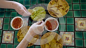 Family hands eating Mexican food corn nachos dipping salsa and avocado guacamole sauce