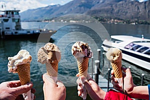 Family hands holding cones of Gelato, Italian ice-cream with blur background of a landscape view of Lake Como in Italy
