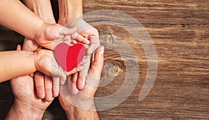 Family hands holding red heart on wooden background. Donation, charity, health concept.