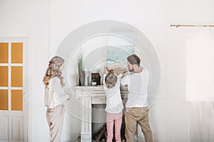 Family hanging picture of sea over the fireplace at home