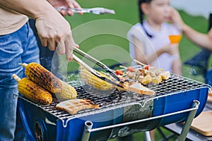 Family happy meal outdoors backyard party BBQ grilled. Roasted meat and corn bread cooking at barbecue stove closeup