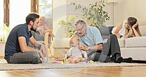 Family happy, satisfied looks at child playing on the carpet with wooden blocks, toddler is