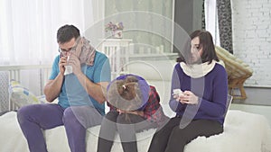 The family has a cold, mom dad and daughter sneeze sitting at home on the bed