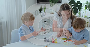 The family has fun painting on paper with their fingers in paint. Mom and two children paint with fingers on paper