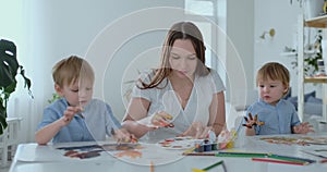 The family has fun painting on paper with their fingers in paint. Mom and two children paint with fingers on paper