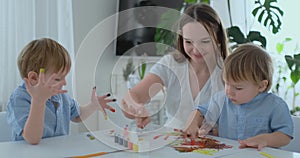 The family has fun painting on paper with their fingers in paint. Mom and two children paint with fingers on paper